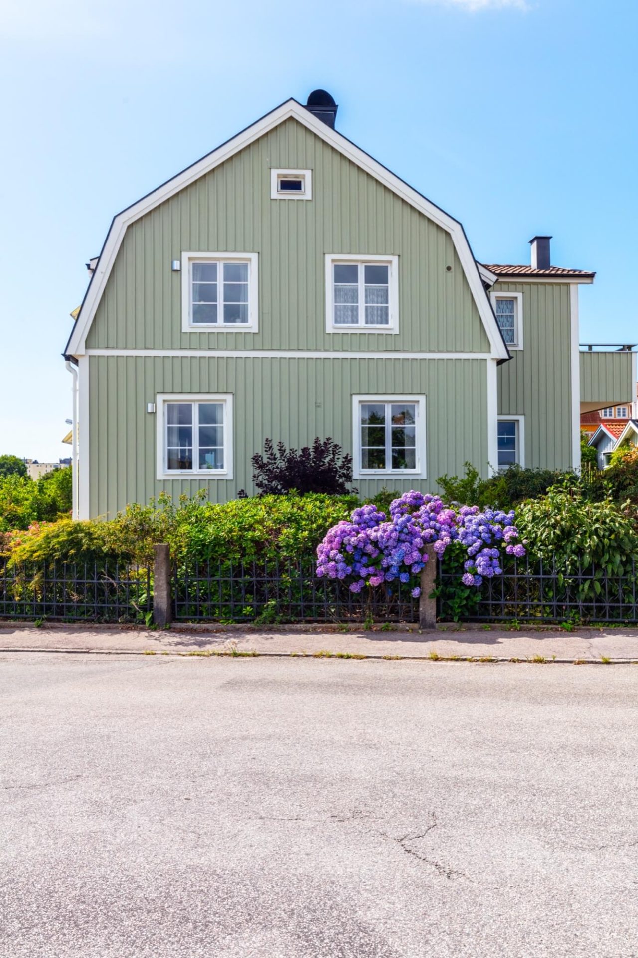 Ett charmigt trähus målat i en livlig grön nyans, accentuerat med vit fasaddekoration och en trädgård sprängfylld med lila hortensior